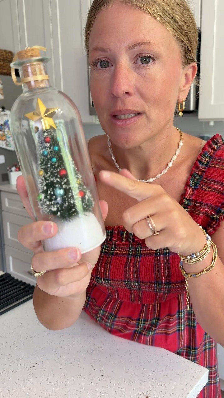 Woman holding a glass bottle with a miniature decorated Christmas tree inside.