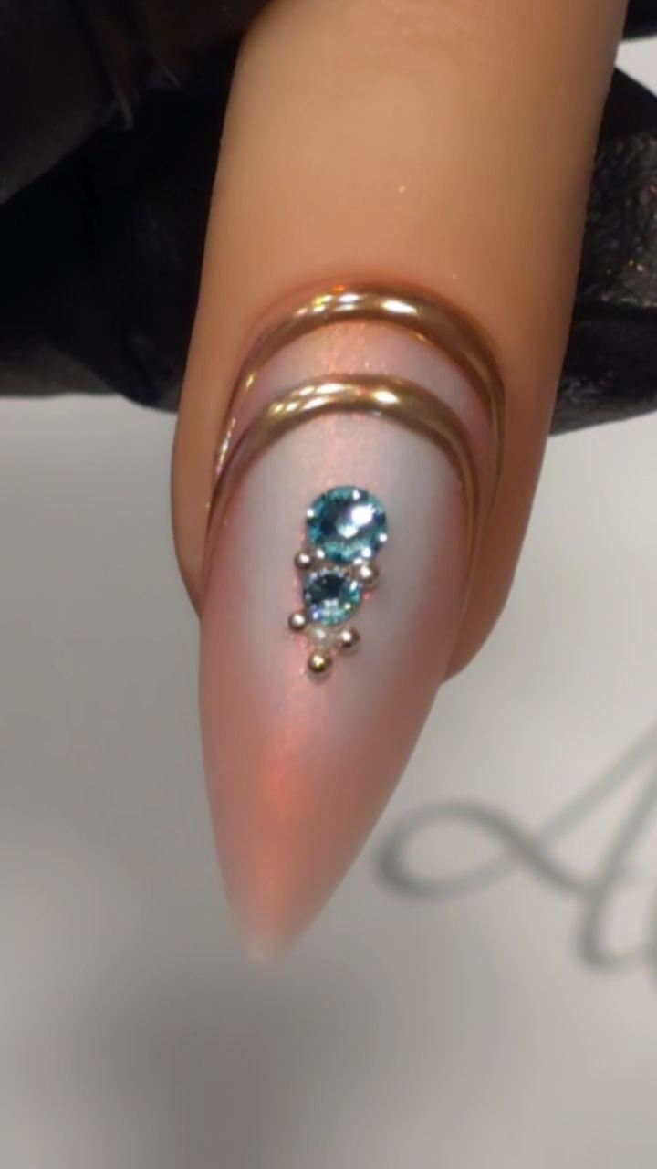 Stiletto nail with pink ombre, gold chrome curved accents, and blue gemstones.