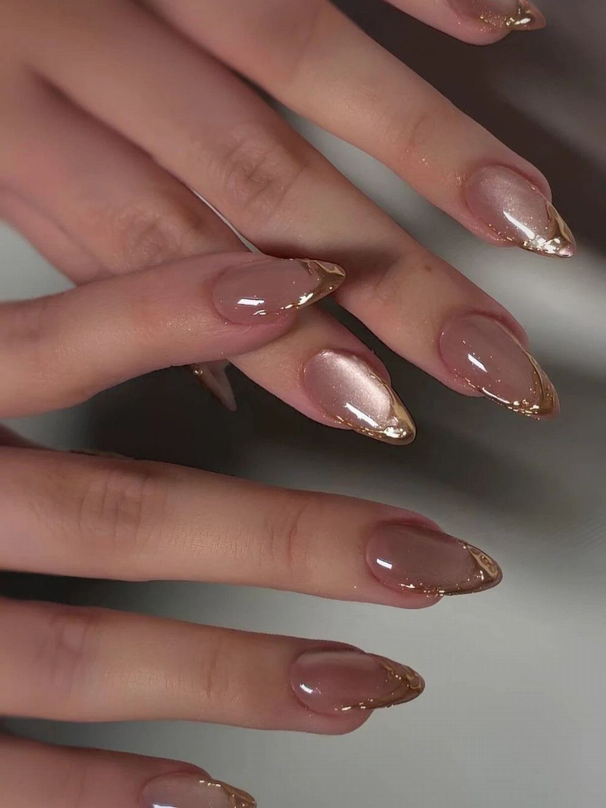 Almond-shaped nails with nude polish and metallic gold chrome French tips.