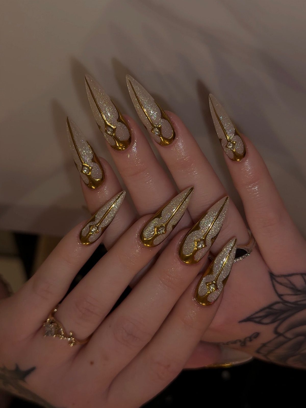 Long stiletto nails with gold glitter and metallic chrome gold swirl accents.