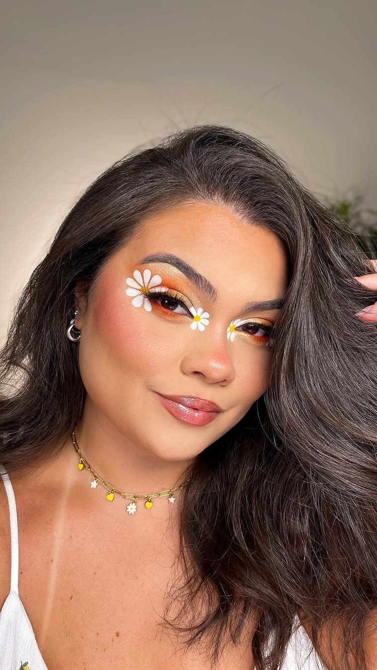 Woman with orange eyeshadow and white daisy flowers painted around her eyes