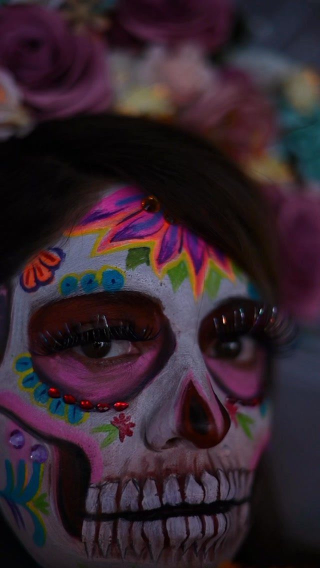 Person with colorful sugar skull face paint and a crown of roses.