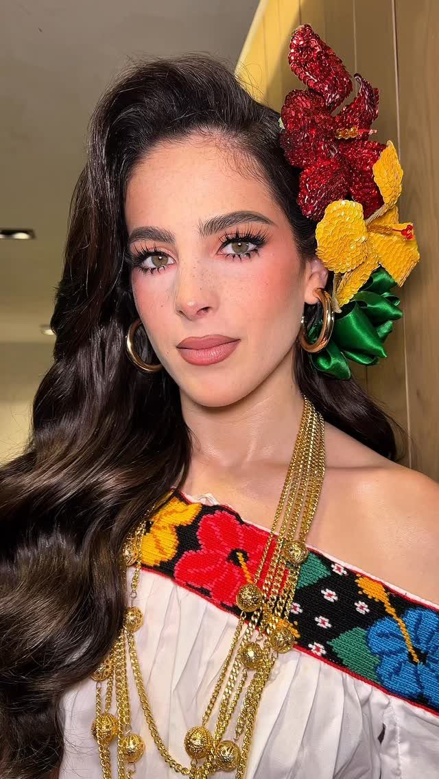 Woman with festive makeup wearing colorful floral hair accessories and embroidered Mexican clothing.