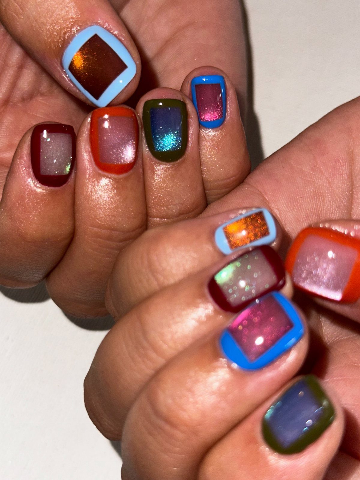Square nails with bold color-blocked borders and shimmering metallic centers in festive colors.