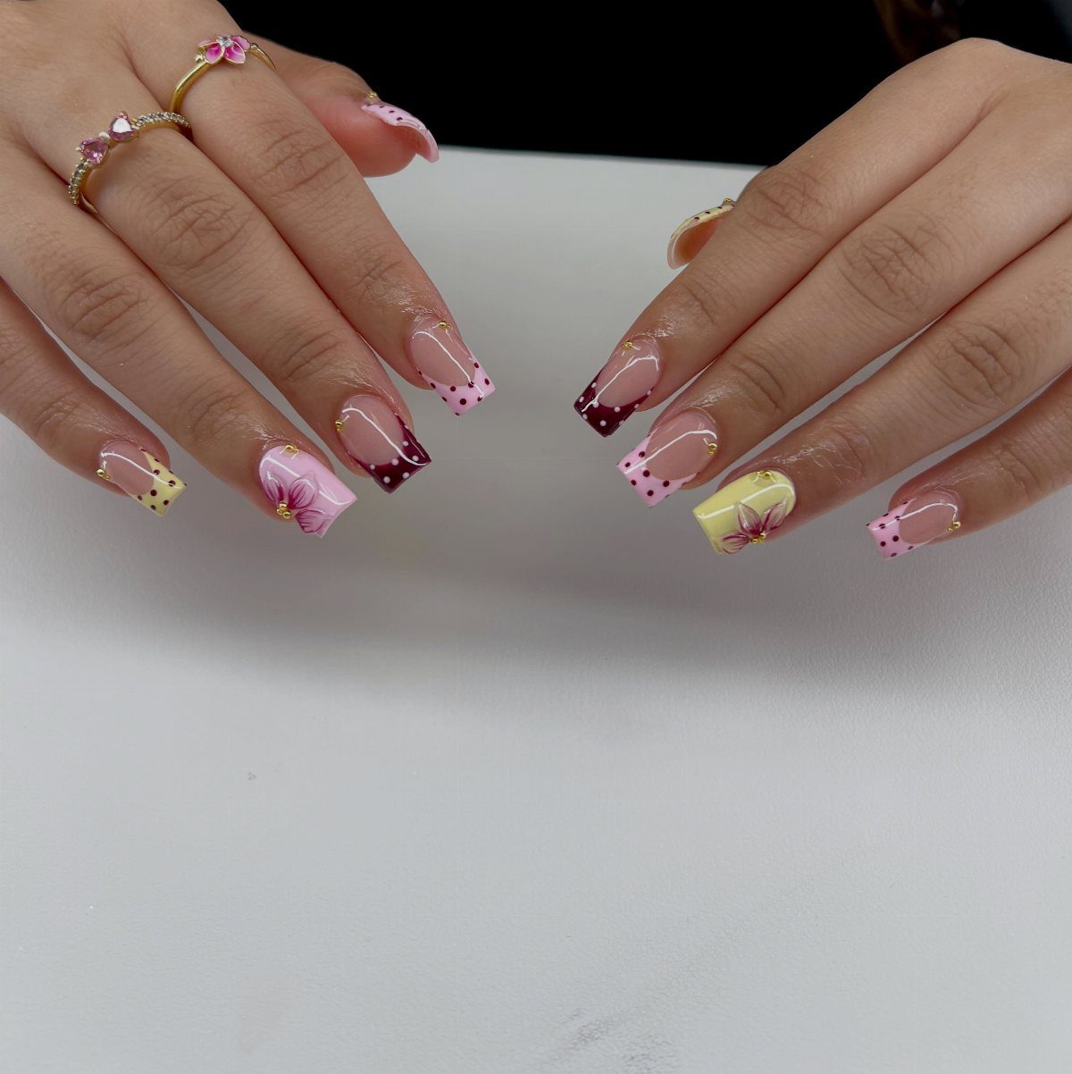 Colorful almond nails with festive French tips, floral art, and gold bead accents.