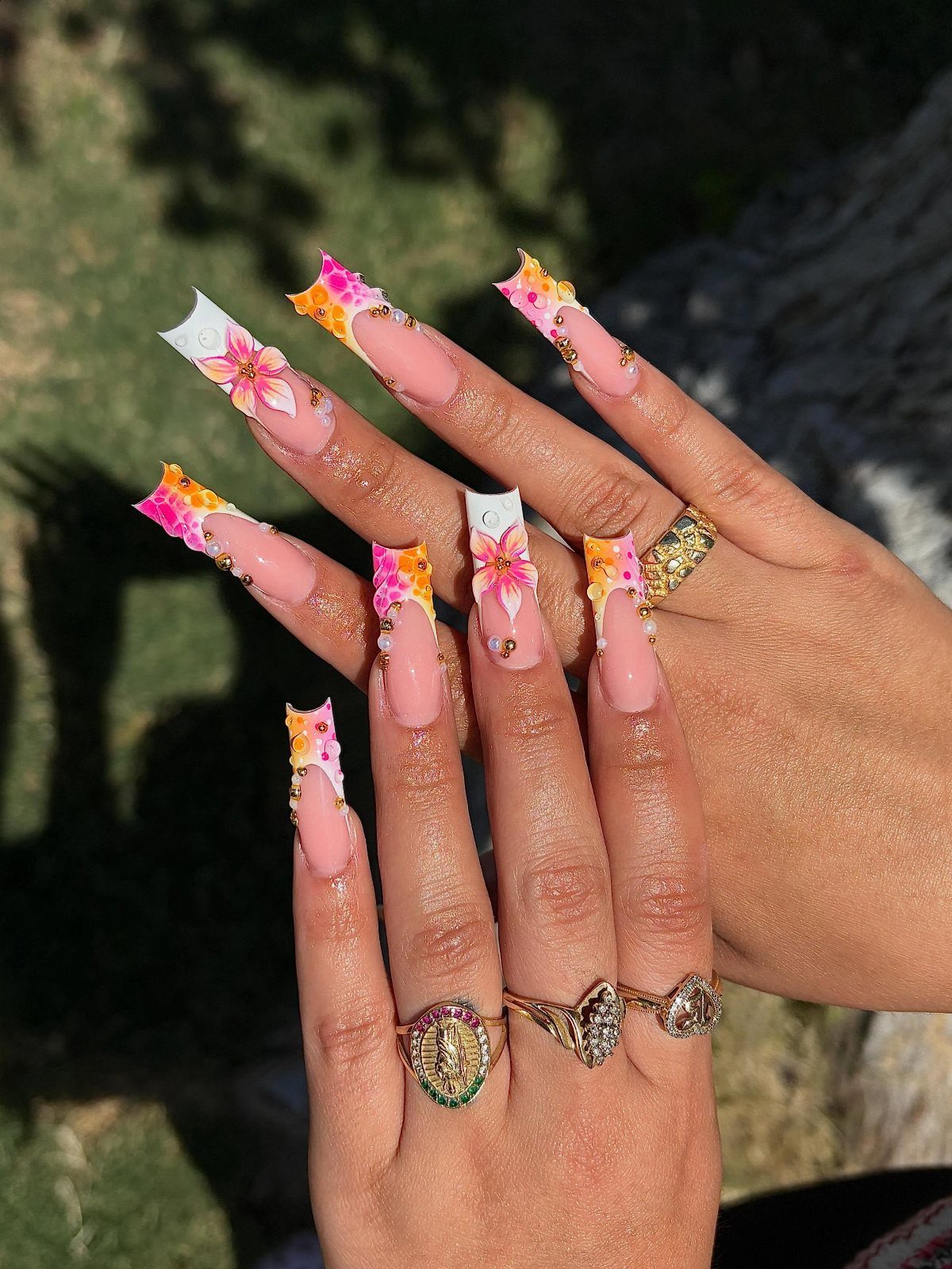 Long coffin nails with vibrant pink and yellow floral art and gold rings.