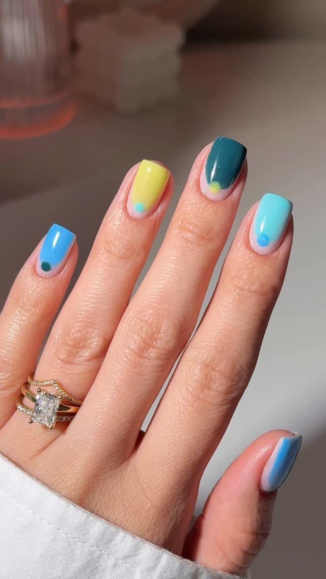 Colorful manicured nails in blue, yellow, and teal with small decorative dots.