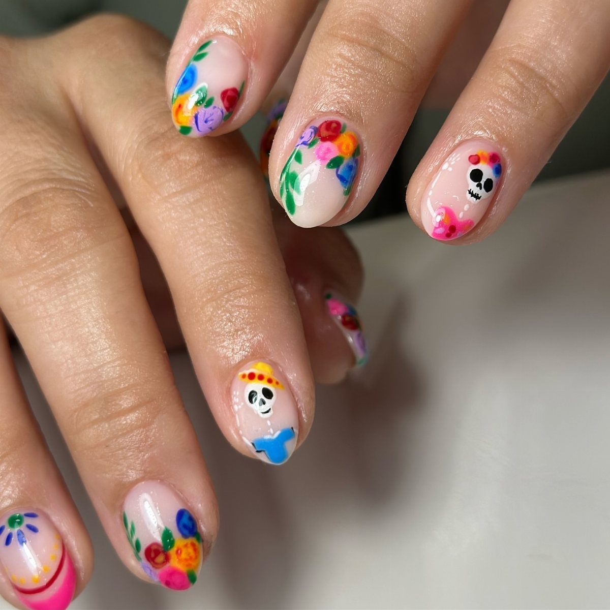 Nude nails with colorful hand-painted flowers and sugar skull nail art designs.