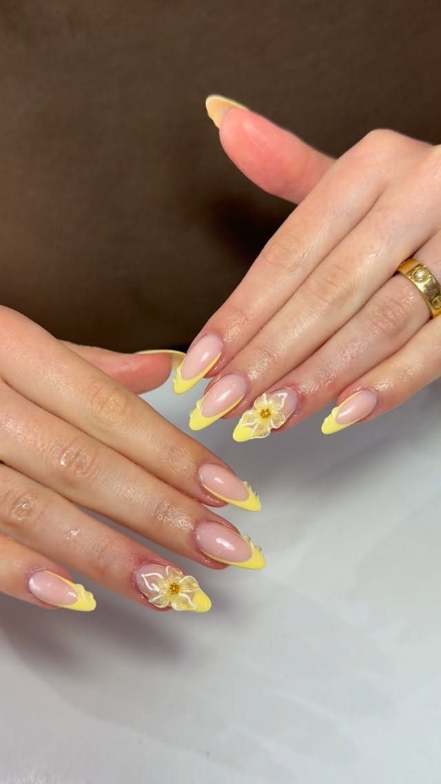 Almond-shaped nails with bright yellow French tips and 3D yellow floral accents.