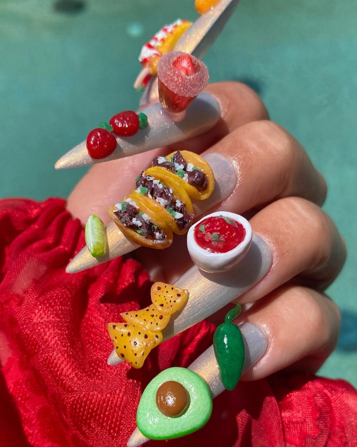 3D nail art featuring miniature tacos, avocado, and salsa on long white nails.