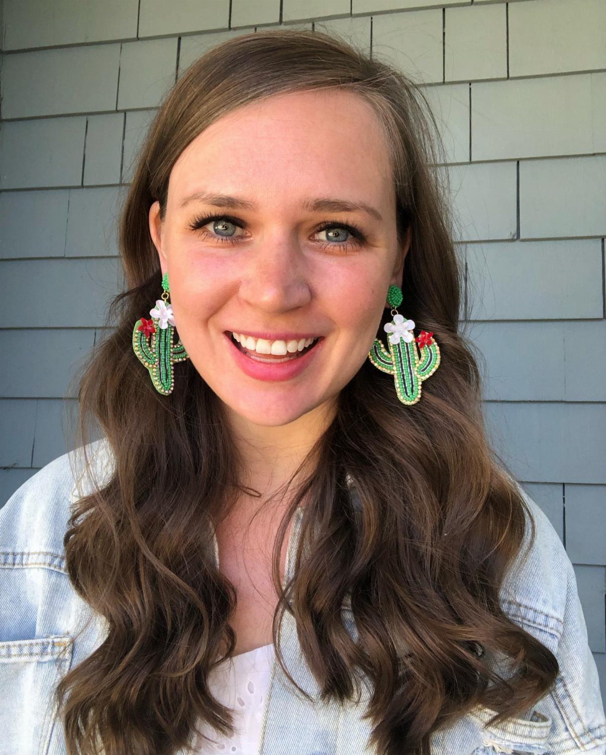 Woman wearing large green cactus statement earrings with small white floral accents.