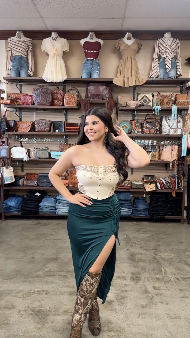 Woman wearing a white corset top, green satin skirt, and cowboy boots.