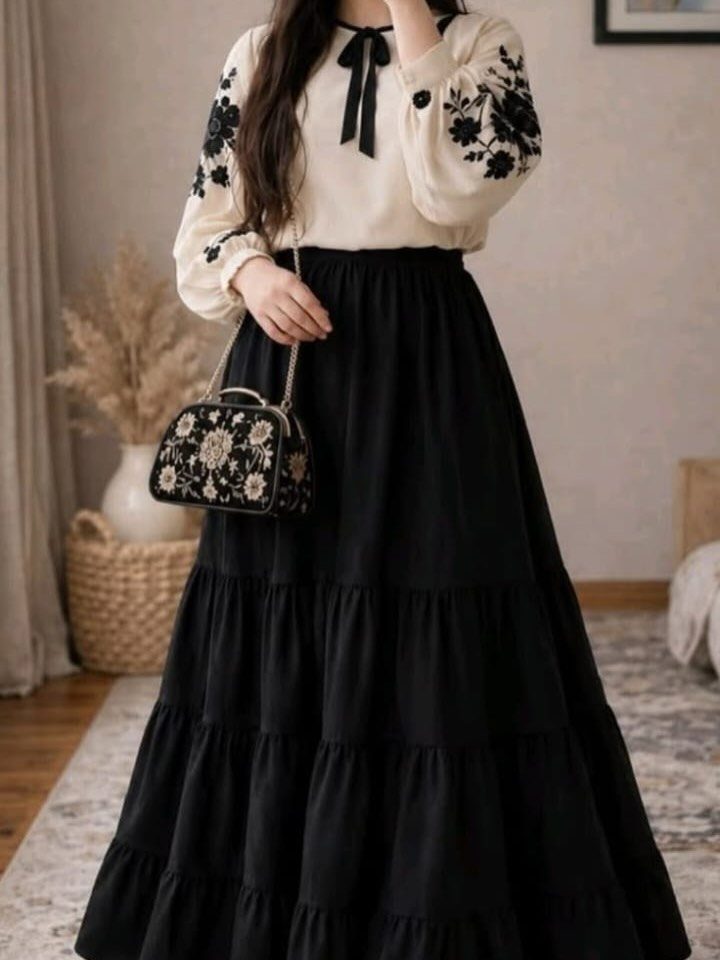 Woman wearing a cream embroidered blouse and a tiered black maxi skirt.