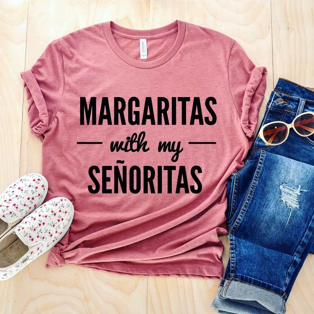 Mauve t-shirt with Margarita text, blue jeans, and floral shoes on wood background.
