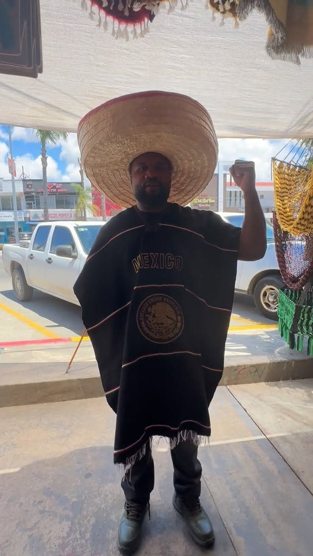Man wearing a large straw sombrero and black Mexican poncho standing outdoors.