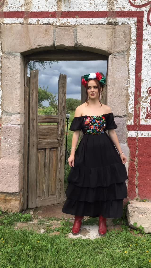 Woman in a black embroidered Mexican-style dress and floral crown standing in stone doorway