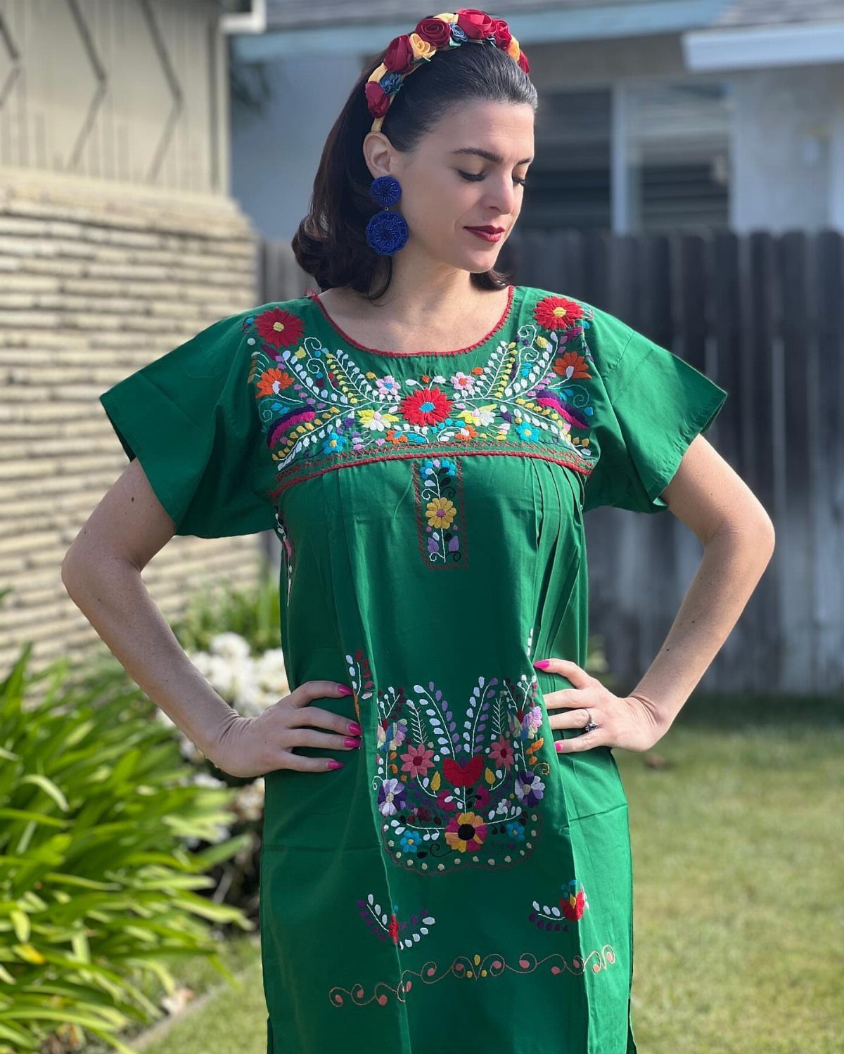 Woman in a green embroidered Mexican dress with floral headband and blue earrings.