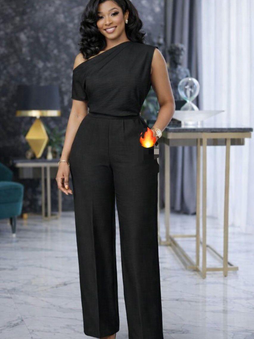 Woman in a black one-shoulder wide-leg jumpsuit posing in a modern interior.