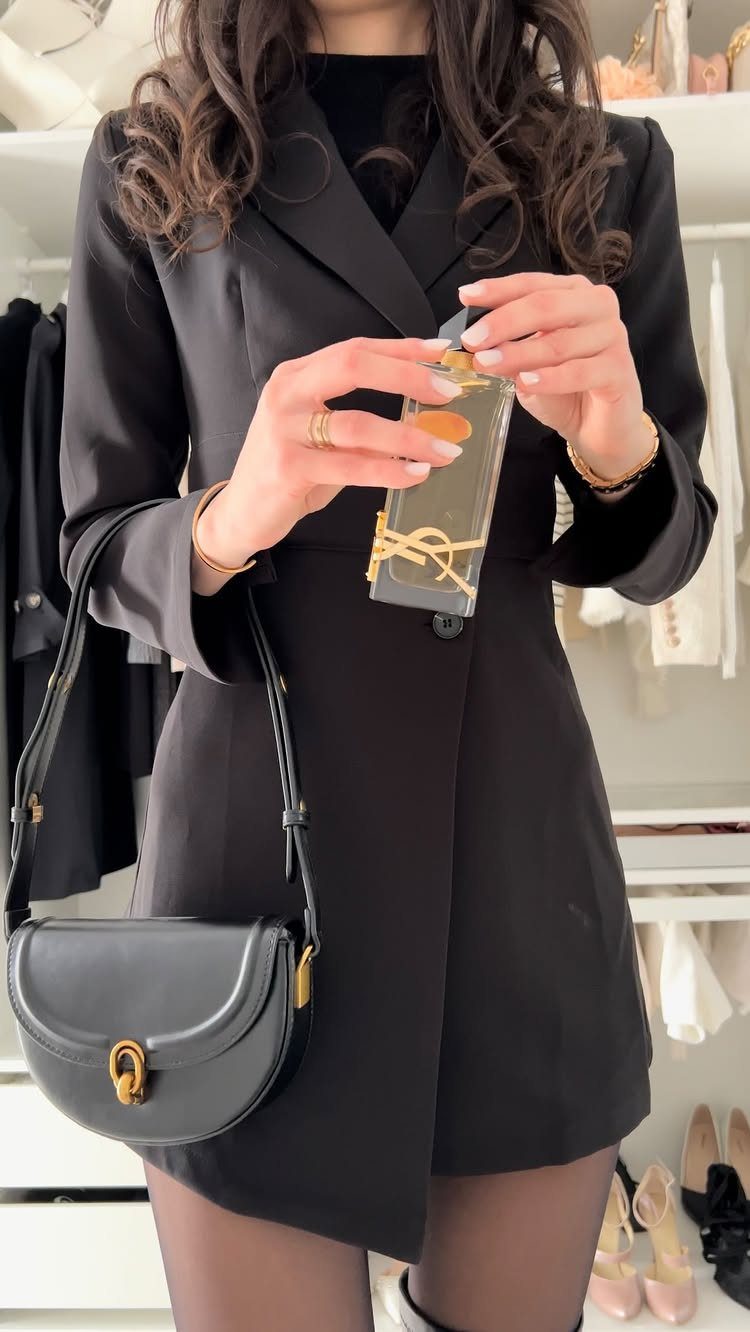 Person in a black blazer dress holding a small gift box in a closet
