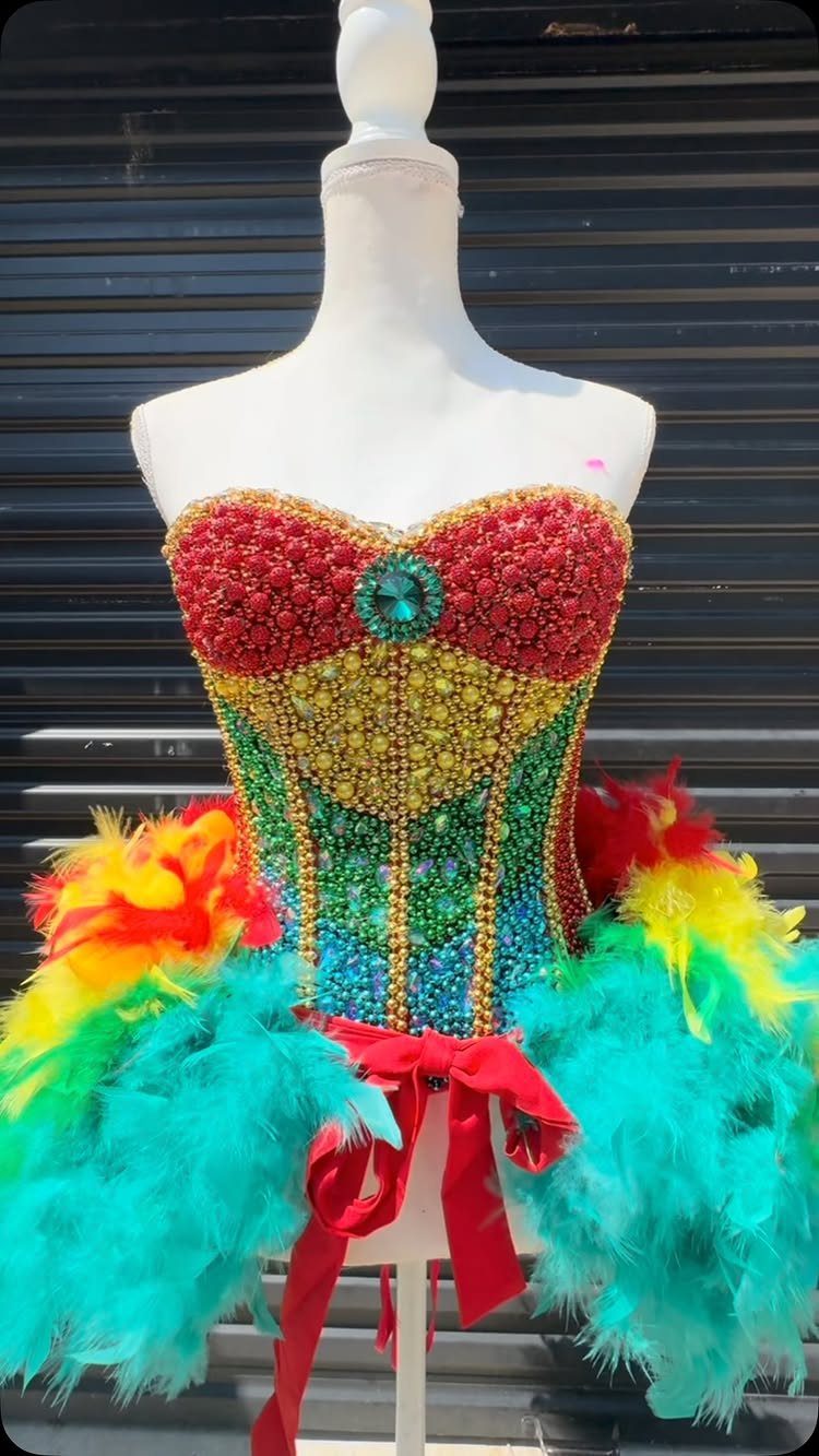 Beaded rainbow corset with colorful feathers on a white mannequin against dark background
