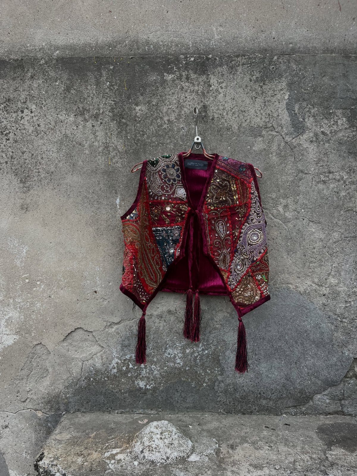 Maroon velvet vest with colorful embroidery and sequins hanging on a grey wall