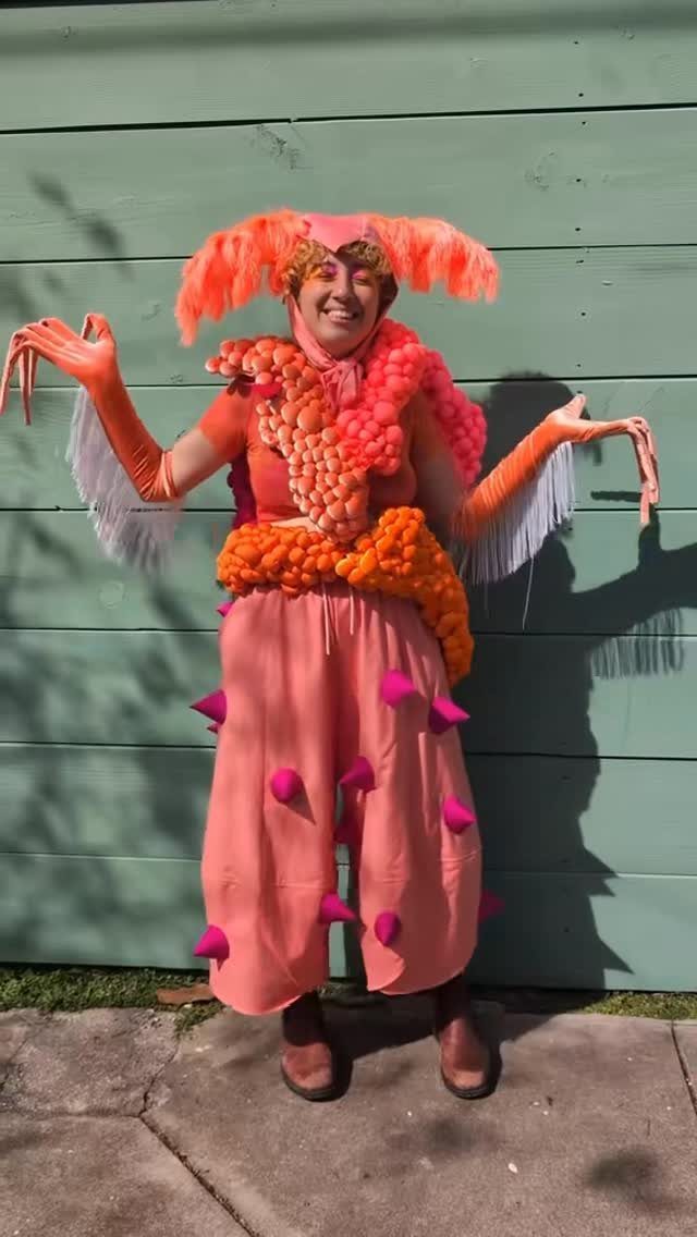 Person in a bright orange shrimp costume with pink spikes and feathered headpiece.