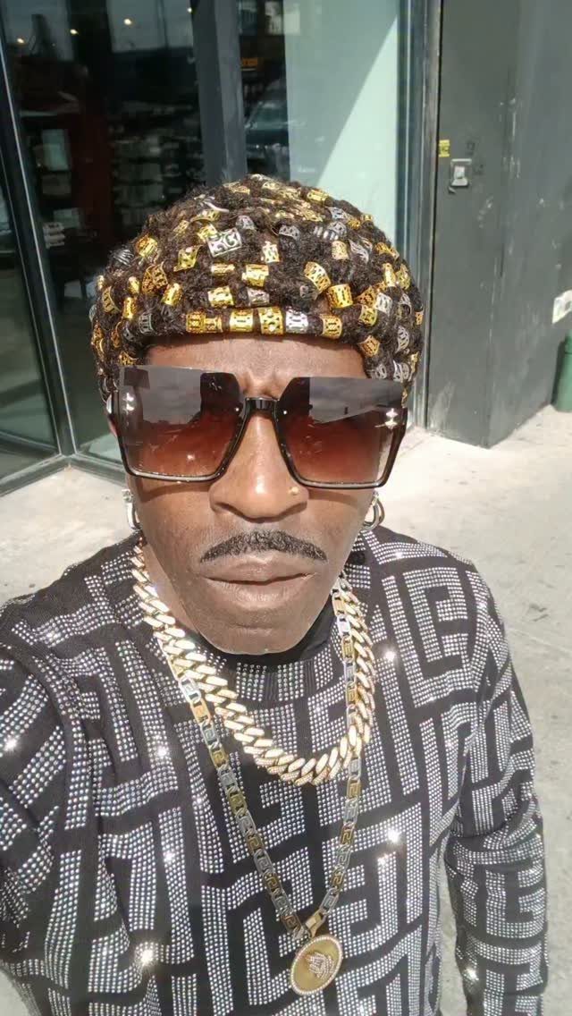 Man wearing a gold-studded hat, large sunglasses, and heavy gold chains.