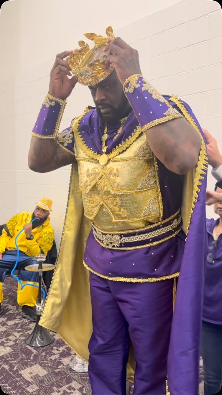 Man in a regal purple and gold king costume adjusting his gold crown.