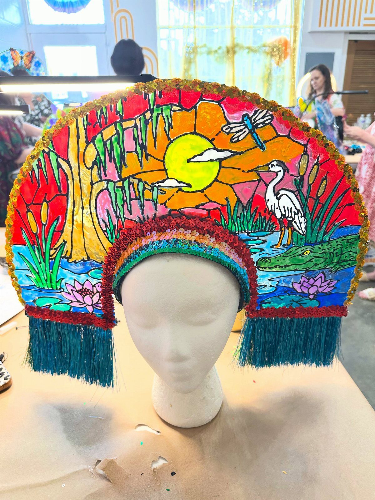 Colorful painted swamp scene headdress with red sequins and teal fringe on mannequin