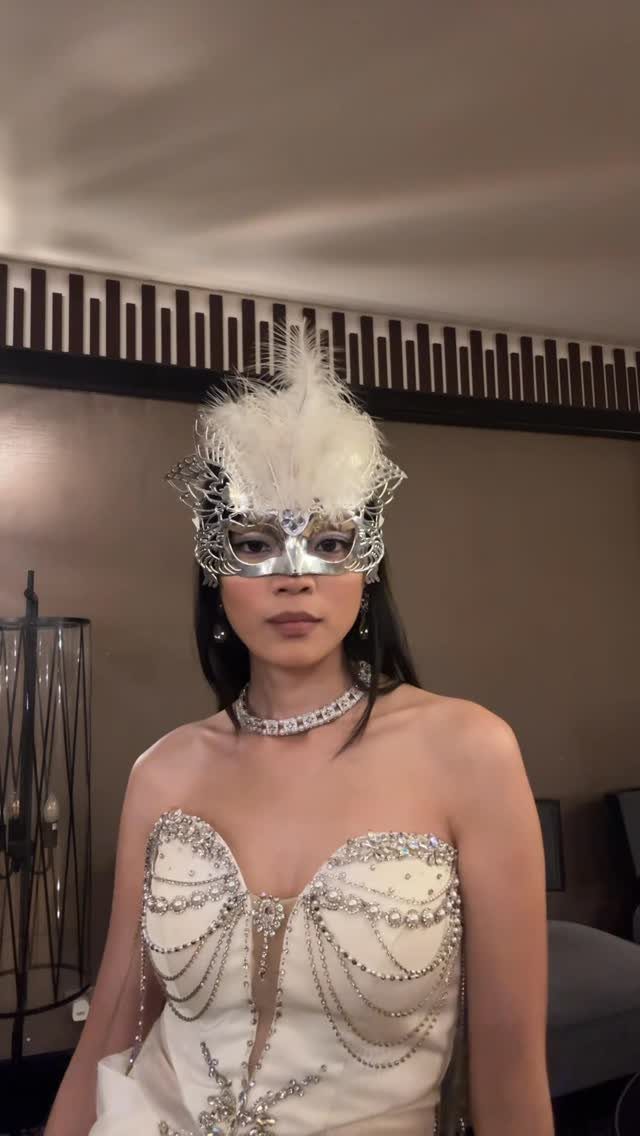 Woman in a white embellished gown wearing a silver feathered masquerade mask