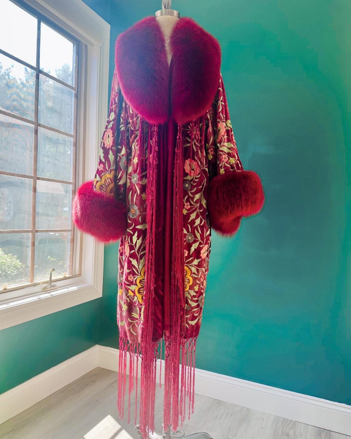 Red and gold floral coat with fur trim and fringe on a mannequin.