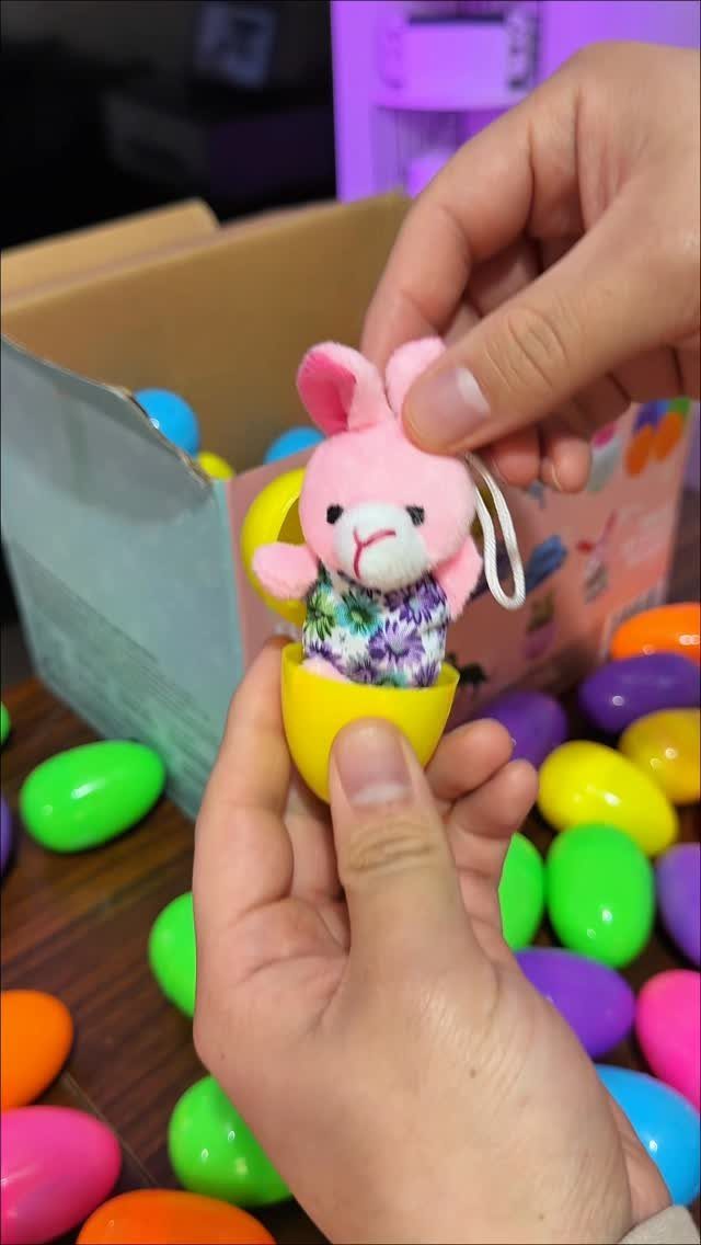 Small pink plush bunny inside a yellow egg surrounded by colorful Easter eggs.