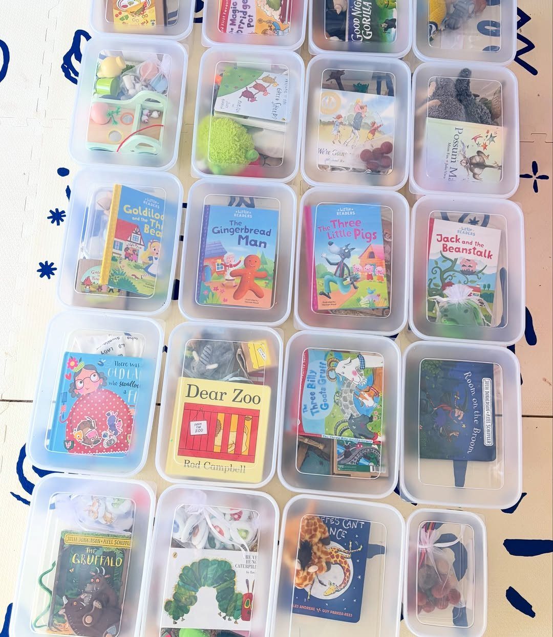 Clear plastic bins containing children's books and small toys arranged in a grid.