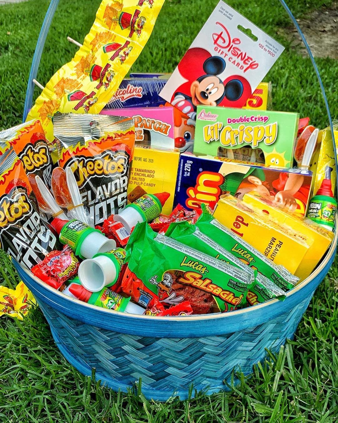 Blue woven basket filled with colorful snacks and a Disney gift card on grass