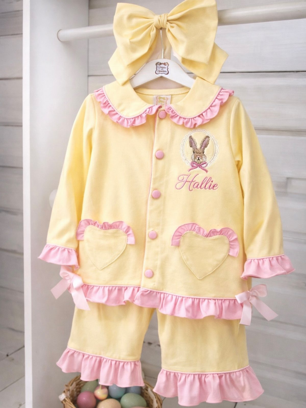 Yellow child's pajamas with pink ruffles and bunny embroidery hanging above Easter eggs.