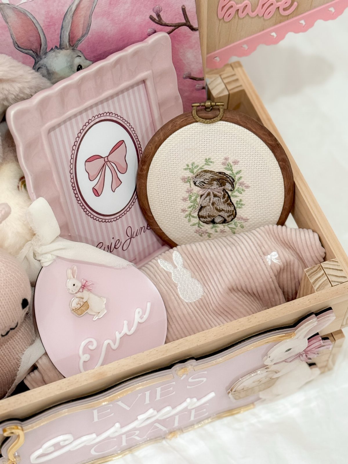 Wooden Easter crate filled with pink bunny-themed gifts, embroidery, and a picture frame.