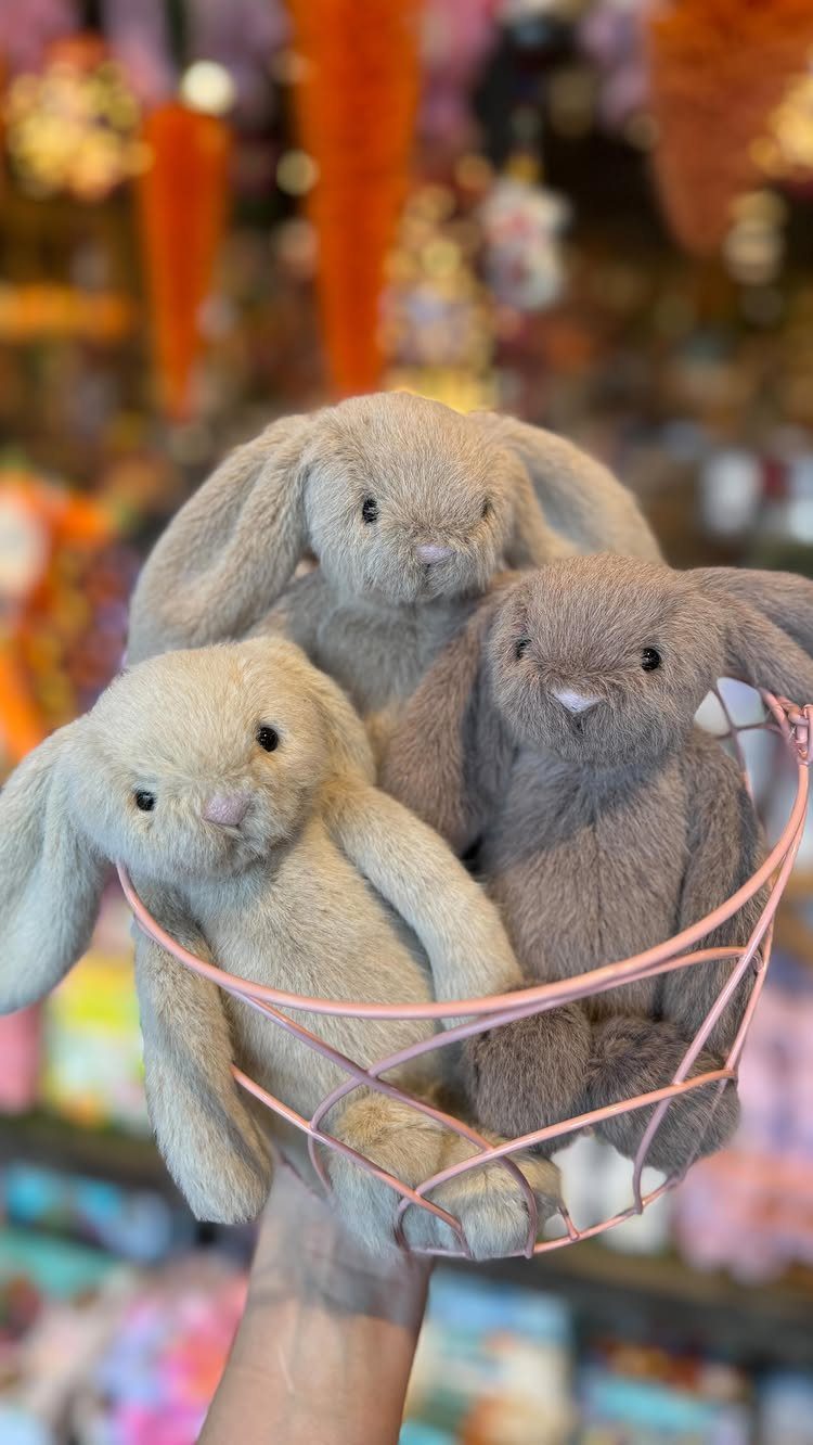 Three plush bunnies sitting in a pink wire basket held by a hand.