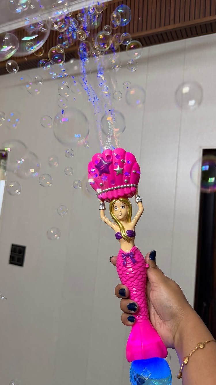 Pink mermaid bubble blower gun emitting iridescent bubbles held by a hand.