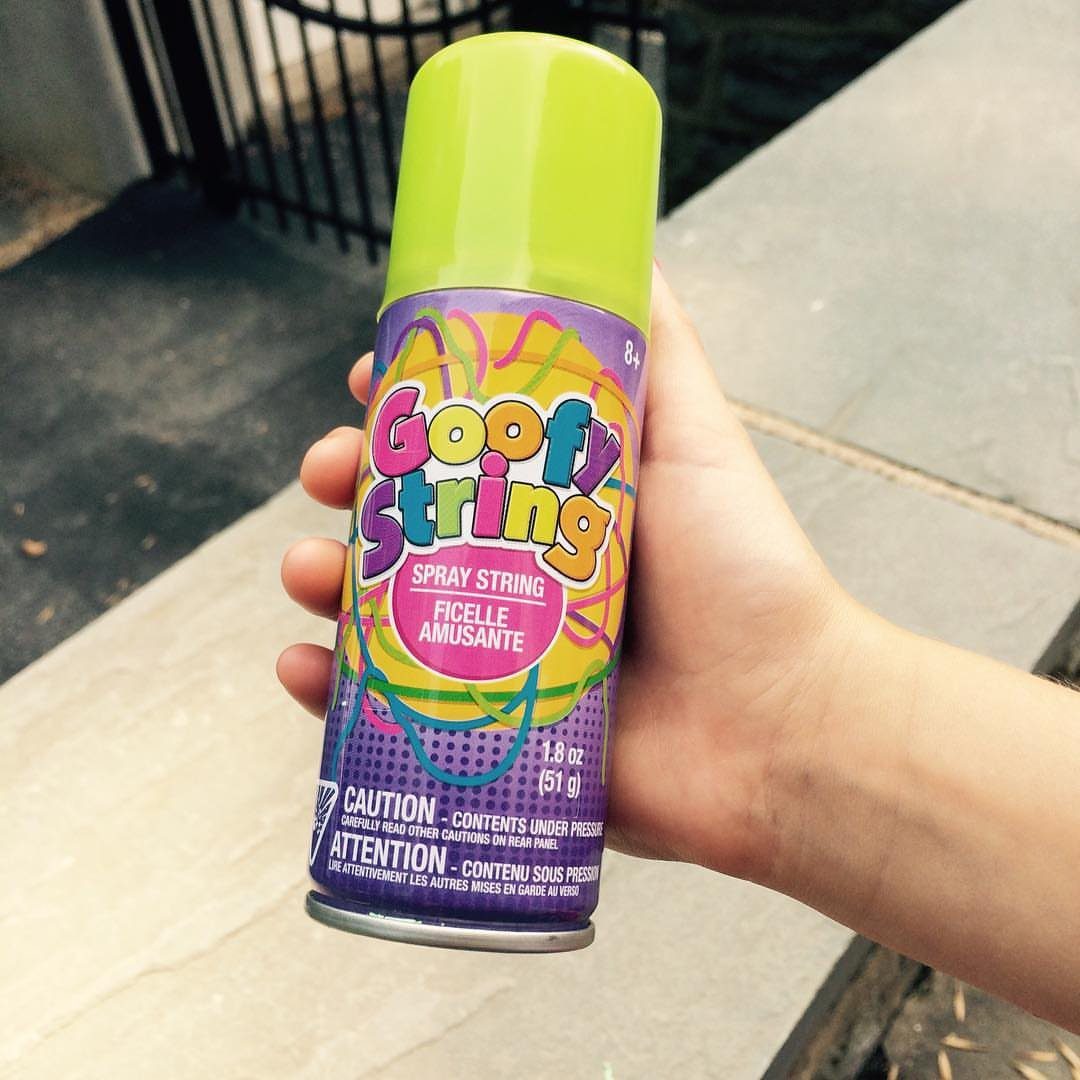 Goofy String spray can held in a hand against a concrete background.