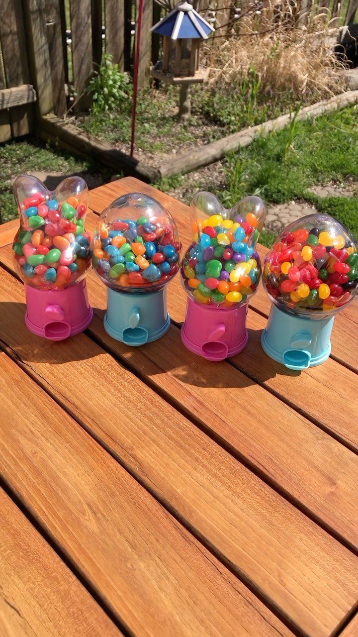 Four colorful candy dispensers filled with jelly beans on a wooden outdoor table