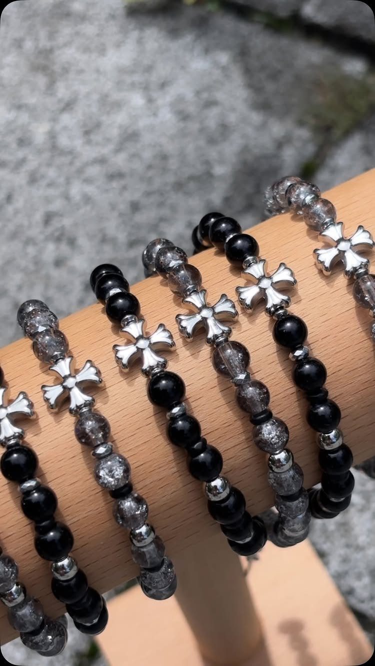 Beaded bracelets with silver cross charms on a wooden display stand.