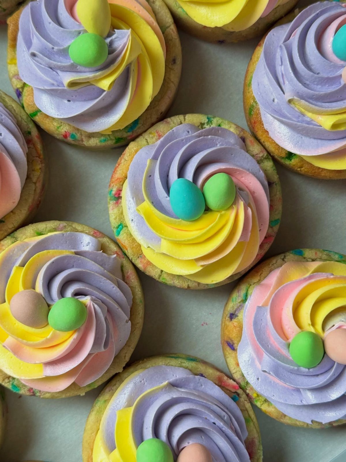 Round cookies with colorful frosting swirls and small candy eggs for Easter treats.