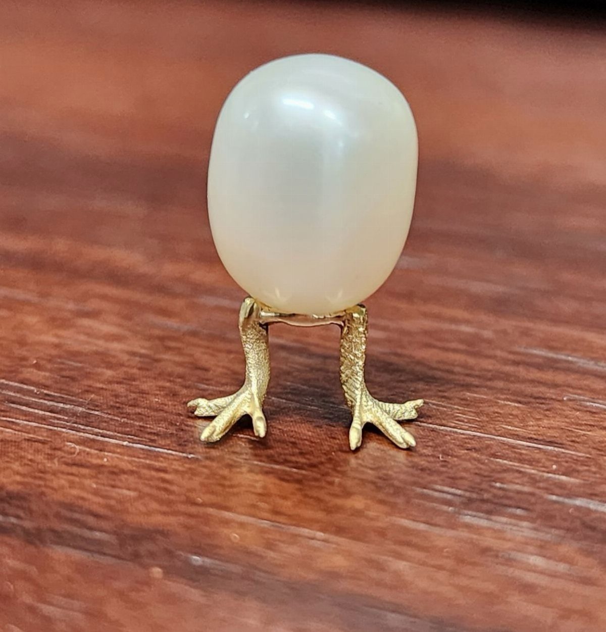 Pearl egg jewelry with gold bird feet on a wooden surface