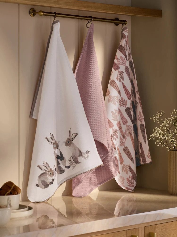 Decorative kitchen towels with rabbit and carrot patterns hanging from a brass rod.