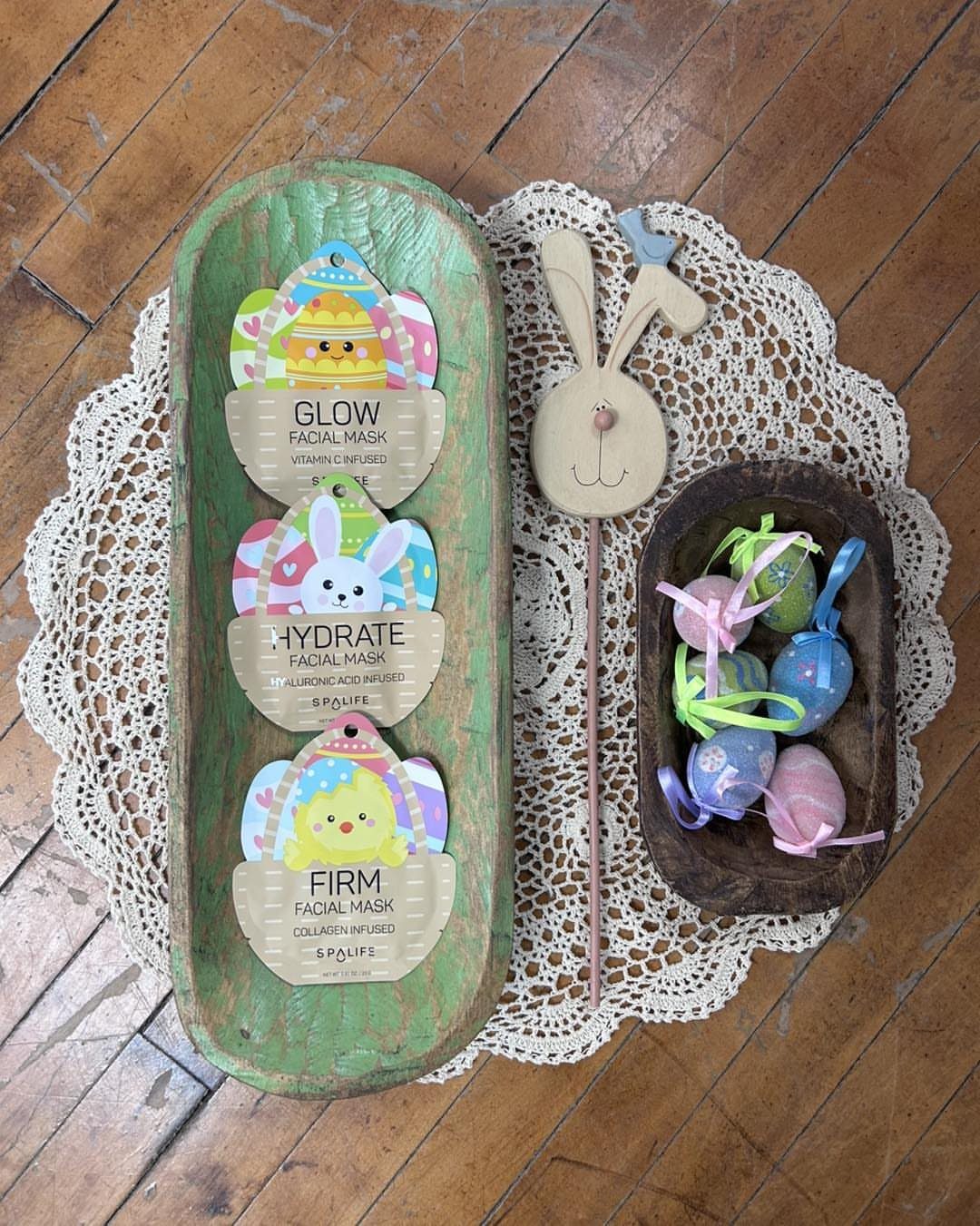 Three Easter-themed sheet face masks in a green wooden tray with colorful eggs.