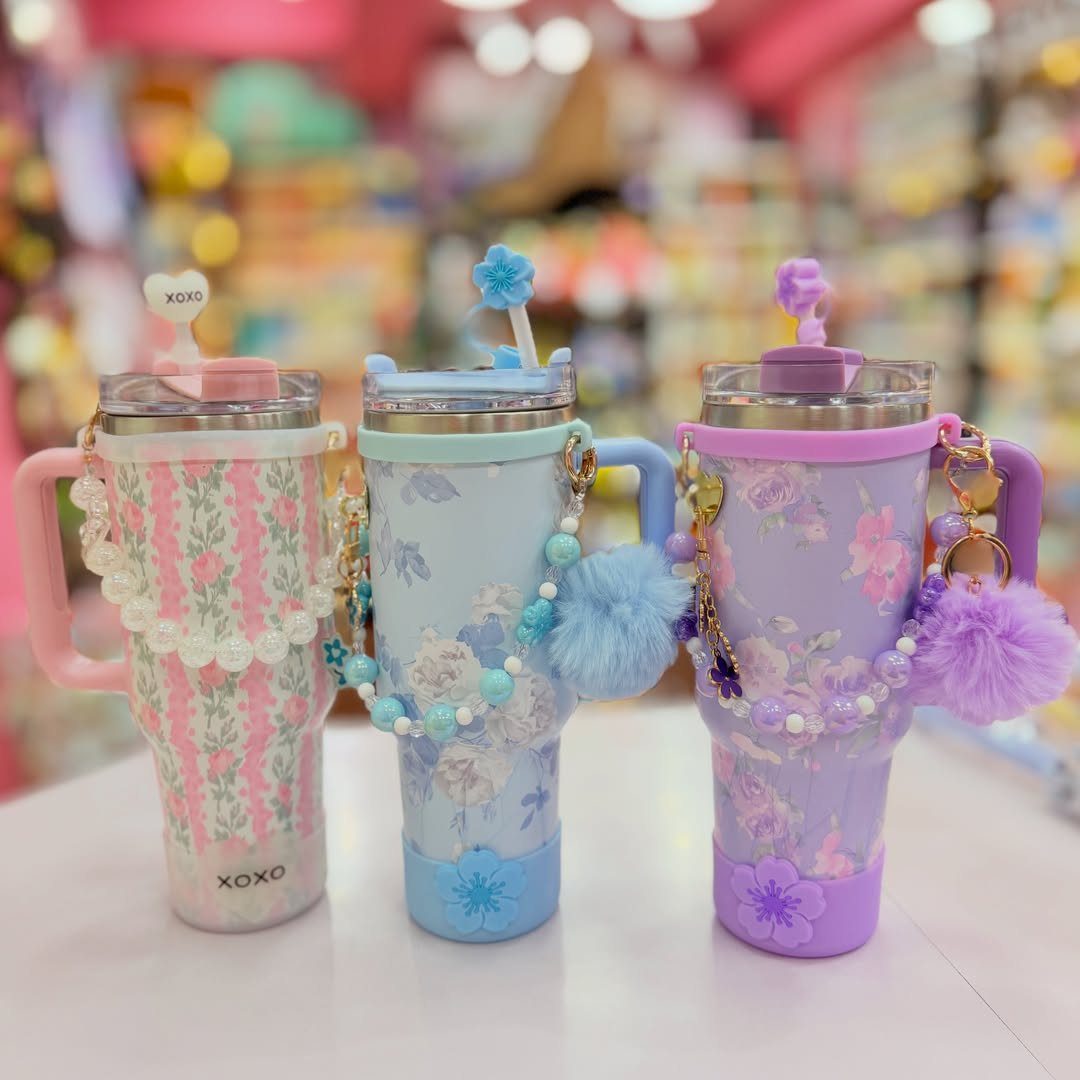 Three floral tumblers in pink, blue, and purple with beaded charms and pom-poms.