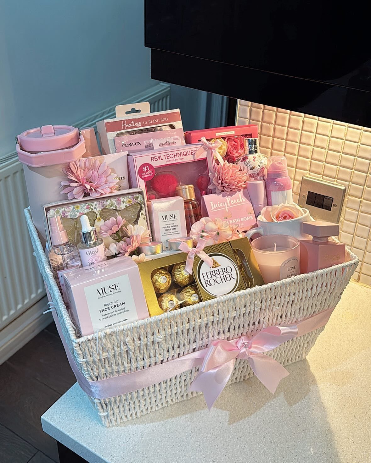 White wicker basket filled with skincare, beauty products, a candle, and chocolates.