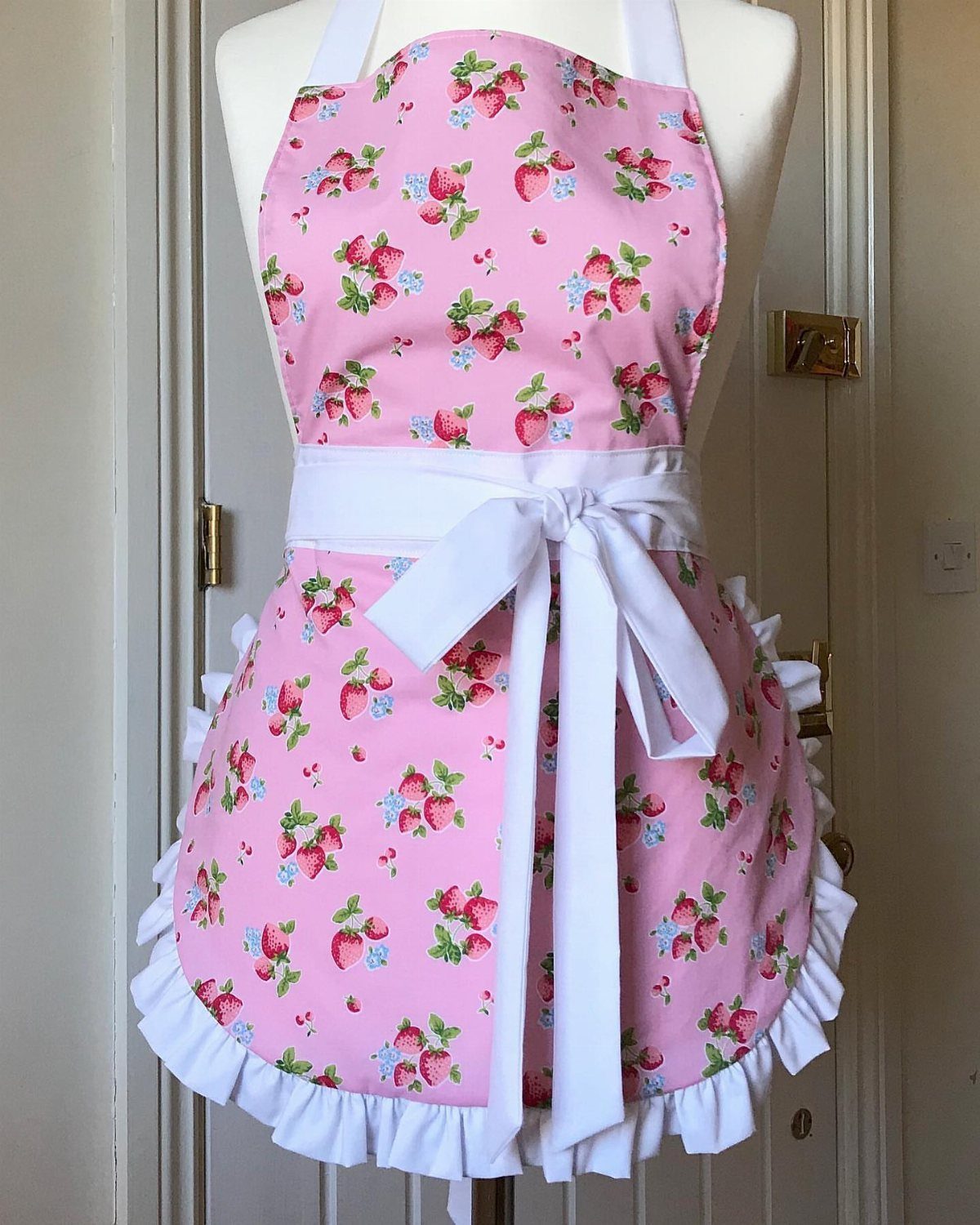 Pink strawberry print apron with white ruffles on a white mannequin