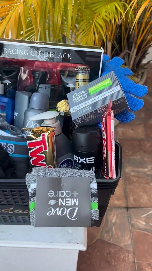 Black gift basket filled with men's toiletries and candy against palm leaves.