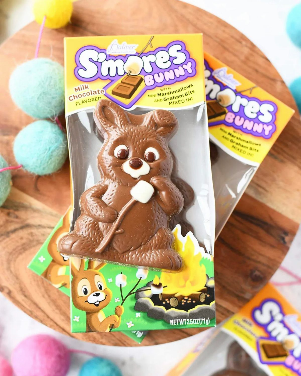 S'mores Bunny chocolate treats in yellow packaging on a wooden board with pom-poms.
